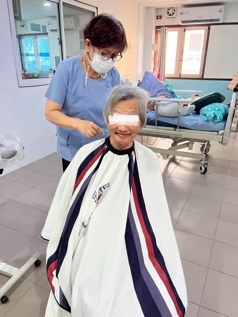 เจ้าหน้าที่ตัดผมให้ผู้สูงอายุข้างเตียงในห้องพัก